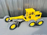 Left side view of Tonka grader showing cab, frame, tires, blade