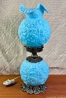 Full view of blue satin glass two-globe hurricane lamp on wood surface