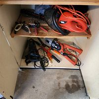 Overview of cabinet showing hedge trimmer, extension cord, hand tools, grinder, reciprocating saw