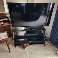 Front view of Samsung 55" TV on stand, remote visible on glass shelf