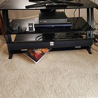 Overall view of TV stand, Sony Blu-ray player on middle shelf, Vizio soundbar on bottom shelf, remotes visible