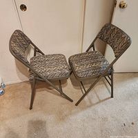 Two gray metal folding chairs arranged facing each other showing fabric pattern and metal frames
