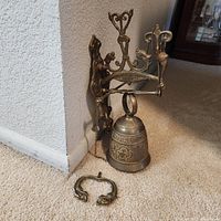 Bell assembly leaning against wall showing bracket, bell body, detached handle