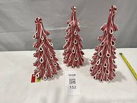 Three red and white resin trees standing upright with tape measure for scale