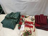 Group shot of all linens including packaged flannel-backed tablecloth, folded green and burgundy napkins, green tablecloth