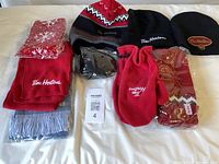 All items laid out: three scarves, three hats, earmuffs, red mittens, packaged acrylic item