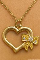 Front view of 14K gold heart pendant with bow and diamonds