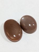 Two brown oval cabochon stones on plain background