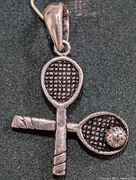 Front view of silver pendant showing crossed rackets and ball