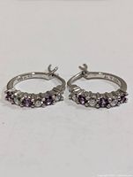 Front view of both sterling silver hoop earrings showing alternating purple and clear stones