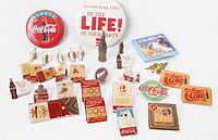 Group shot of all 30 Coca-Cola pins and buttons displayed on white surface