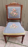 Full front view of chair showing carved frame, needlepoint upholstery and casters