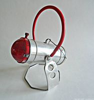 Left front three-quarter view showing aluminum body, red rear lens, red handle, metal stand