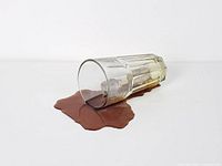Side view of glass tumbler lying on brown resin spill