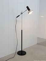 Full view of black and chrome adjustable angle-poise floor lamp standing on circular base