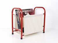 Front angled view showing red metal frame, white canvas sling, magazines for scale