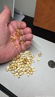 Hand holding and desk showing pile of oval citrine cabochons with coin for scale