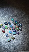 Group of small oval black opal cabochons on textured surface