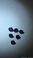 Six loose round blue sapphires on white surface