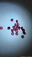 Cluster of loose round pink-red garnets under spotlight