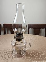 Front view of complete clear glass oil lamp showing base, burner, chimney and finger loop