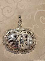 Front view of ornate silver sifter showing pierced bowl and figure motif