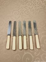 Six matching butter spreaders laid out showing stainless blades and ivory handles