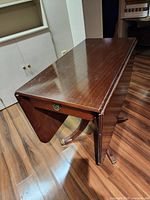 Overall view of dark wood drop-leaf table with one leaf down showing pedestal base and brass feet