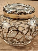Front and top view of glass vanity jar highlighting silverplate filigree and overall shape