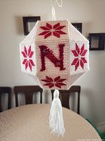Overall view of the handmade plastic canvas NOEL ball showing letter N, red star motifs, hanging loop, tassel