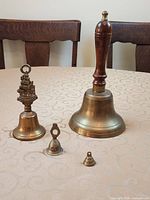 Four brass hand bells of varying sizes on table