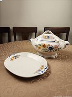 Front view of tureen with lid and ladle beside matching bread plate