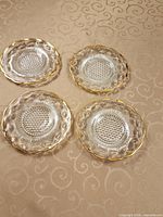 Top view of four clear pressed glass plates with gold rims arranged on patterned surface