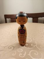 Front view of the single wooden Kokeshi doll standing on table showing painted details