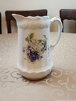 Full view of white ceramic pitcher with violet and hydrangea design showing shape, handle, rim and floral decoration