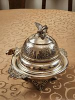 Front view showing domed lid, butterfly finial, floral engraving, stand and spreader