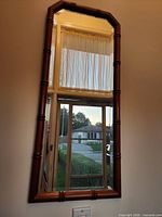 Overall front view of vertical wall mirror with faux-bamboo style wooden frame