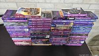 Front view of six tall stacks of purple-spine paperback romance novels with two books laid horizontally on top
