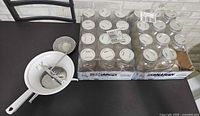 Two cases of Bernadin 1 L mason jars and food mill on table