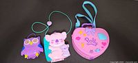 Closed view of three Polly Pocket compacts: owl, koala with lanyard, heart shaped