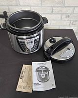 Cooker base with inner pot, lid and manuals on tabletop