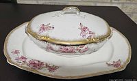 Covered serving dish with lid on underplate showing floral pattern and gold trim