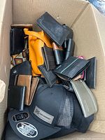 Top view of box showing multiple wallets, pouches, orange purse and black DC Shoes cap