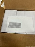 Open box showing stacks of white window envelopes with one envelope displayed on top