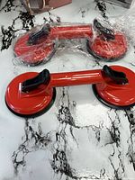Two red double suction cup lifters, one unwrapped, one partially wrapped