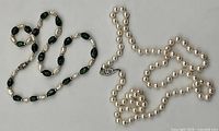 Two necklaces laid flat showing green stone and rice pearl strand and round pearl strand with clasps