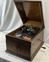 Phonograph with lid open showing turntable, tonearm, crank and record on platter