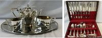 Grouped view of silver-plated tea service on tray beside opened flatware chest showing utensils
