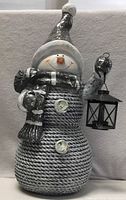Full view of snowman statue showing body texture, hat, scarf, and lantern