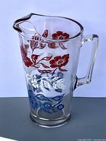 Full view of clear glass pitcher showing handle, spout and multicolor floral decoration